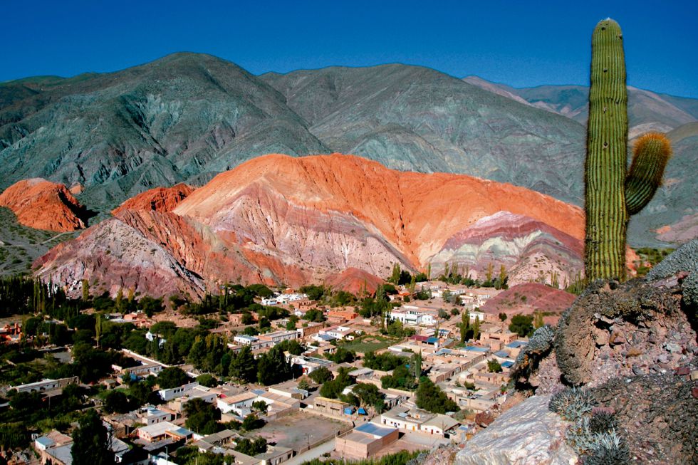 Purmamarca se encuentra al pie del Cerro de los Siete Colores, que debe su nombre a la policromía resultante de sedimentos marinos, lacustres y fluviales acumulados durante más de 600 millones de años. Disfrutar de los tonos de rojo, rosa, gris, blanco y verde del cerro justifican la visita al pueblo. Sus casas bajas de adobe y sus calles de tierra convierten a Purmamarca en el pueblo más pintoresco de la Quebrada de Humauaca, en la provincia de Jujuy, una región de fuertes raíces quechua y aimara. La población, de sólo 500 habitantes, se ha habituado poco a poco a la presencia de turistas sin perder el ritmo sosegado y silencioso de la Puna.