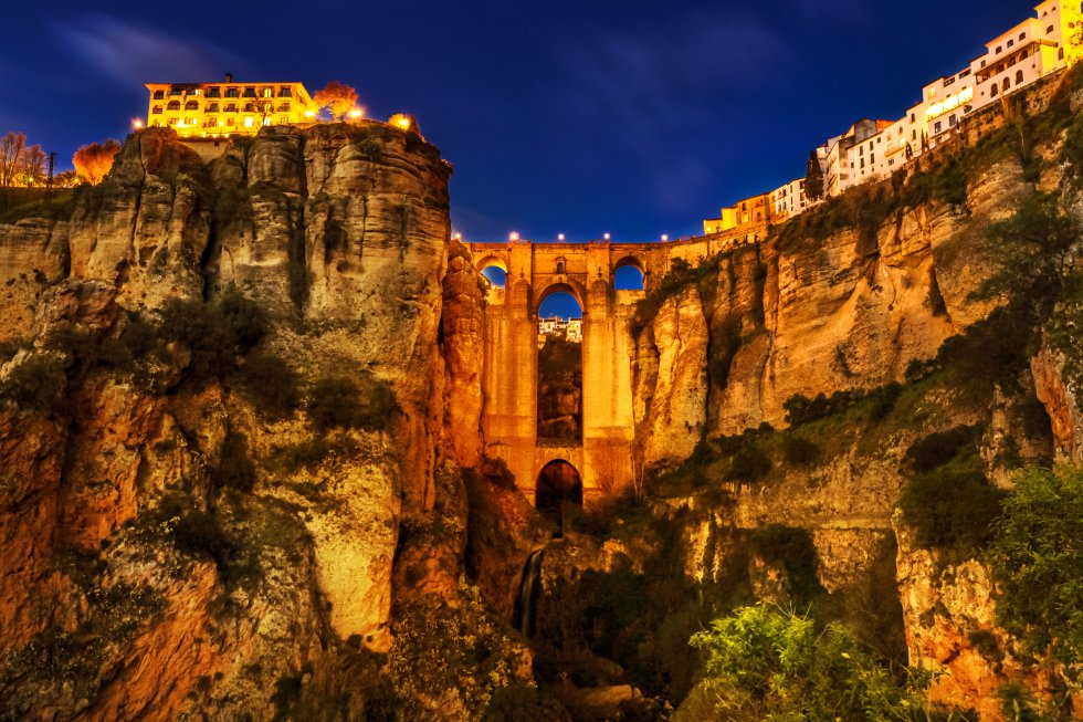 Los mejores lugares para asomarse al Puente Nuevo de Ronda son los miradores de la Plaza de España y la calle de Ernest Hemingway, en la parte nueva, justo a la entrada del puente, santo y seña de  esta ciudad malagueña  junto a su plaza de toros de la Real Maestranza de Caballería. Tuvo un primer intento de construcción en 1735, que se derrumbó seis años después, y un segundo, exitoso, en 1751, que finalizó en 1793 y dejó para la historia esta gran obra de sillares de piedra y 98 metros de altura, que une las dos mitades de un casco urbano partido por un Tajo y no es apta para quienes sufren vértigo.