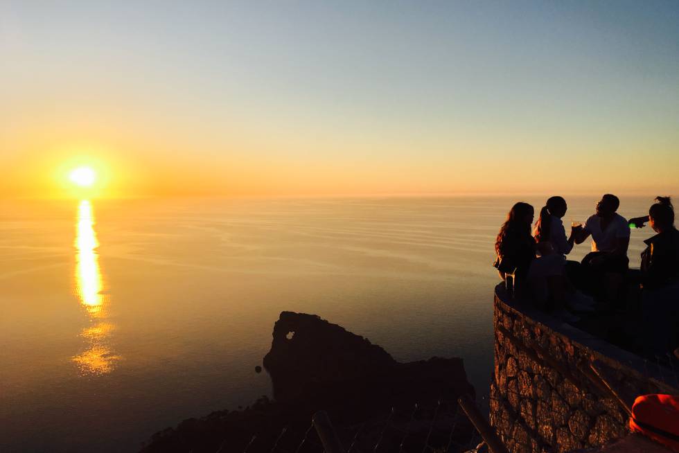 La puesta de sol congrega a viajeros y turistas en el Mirador Sa Foradada, entre la cala de Deià y el caló de S'Estaca, en  la costa oeste de Mallorca , inmerso en el paisaje espectacular de la Sierra de la Tramuntana y con vistas a un curioso (y conocido) accidente geográfico de la isla: una pequeña península que se adentra en el mar, con la roca agujereada (foradada) que le da nombre en su parte final, y que ha servido de inspiración a viajeros y artistas. Es un clásico asomarse a este balcón para hacerse un selfie o disfrutar de la postal desde la terraza del restaurante Na Foradada  (naforadada.es) .