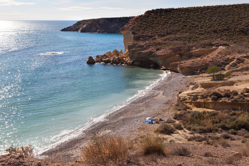 Su relevancia tiene que ver con las formas que el Mediterráneo puede dar a una línea de acantilados semidesérticos. Entrando por Puntas de Calnegre (en la foto), la primera cala en este tramo del parque regional de Cabo Cope y Puntas de Calnegre lleva por nombre, precisamente, Calnegre. Su arena dorada contrasta con la pizarra y es (avisa su bandera azul) la más frecuentada, amén de la más arriesgada: con levante fuerte se forman remolinos a la altura del chiringuito El Líos (recomendable reservar la paella, a partir del 16 de junio, en el 620 02 97 86). Las reducidas dimensiones, la arena fina, el abrigado entrante del mar y la limpieza de sus aguas hacen de Baño de las Mujeres —la siguiente cala— un lugar de referencia. De continuar a El Siscal, el bañista encontrará un amplio varadero, hoy sin pulsión marinera. Si todavía no ha reparado en las comunidades de azucena de mar, es el momento de buscarlas (y respetarlas). Acceso: 1 kilómetro antes de Puntas de Calnegre sale la pista de 2,5 kilómetros que muere en la cala de El Siscal. Este verano hay previstas restricciones de acceso los fines de semana.