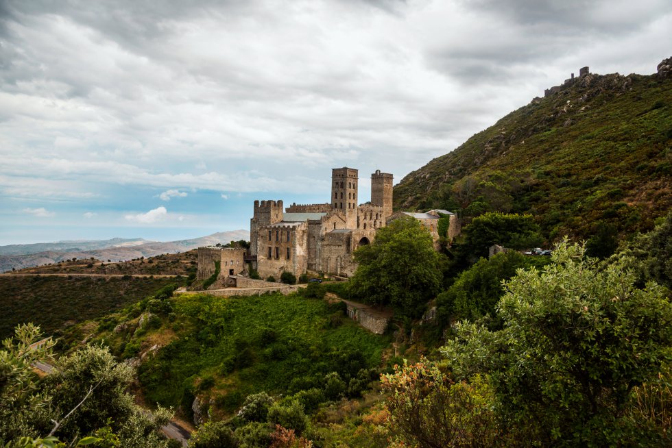 Aparece citado por primera vez como comunidad religiosa en el año 879, en el siglo X comienza a construirse la abadía y en 1022 se consagra la actual iglesia. Su compleja estructura, con tres niveles superpuestos, es inédita en el románico español y parece inspirarse en las monumentales fachadas romanas, según dice Jaime Cobreros, autor de la guía  'Los mejores destinos del Románico en España' , publicada por Anaya Touring. El claustro es el eje central de este conjunto alzado sobre la falda de la montaña, con vistas a la bahía de Llançà y al Port de la Selva (al norte del cabo de Creus). La perfección de sus capiteles corintios hace pensar a los expertos en magníficas copias, o incluso en piezas romanas auténticas.